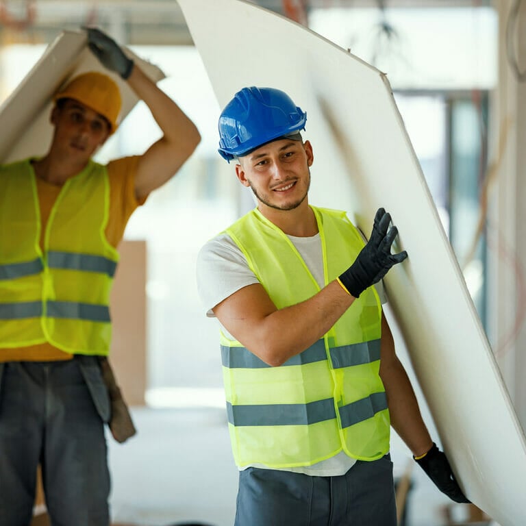Construction workers carrying drywall.
