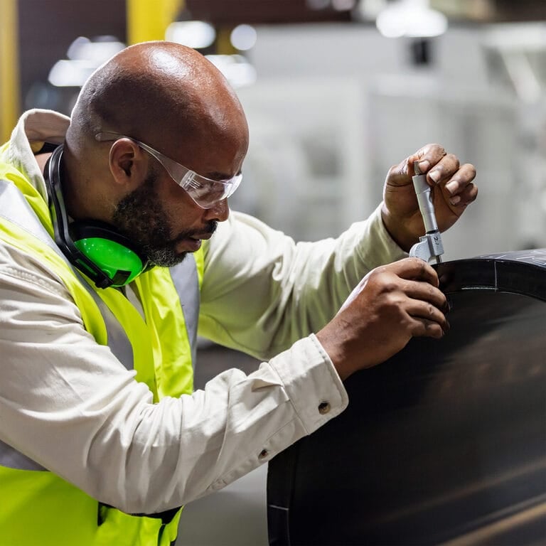 A temporary quality inspector uses a caliper to measure an industrial part.